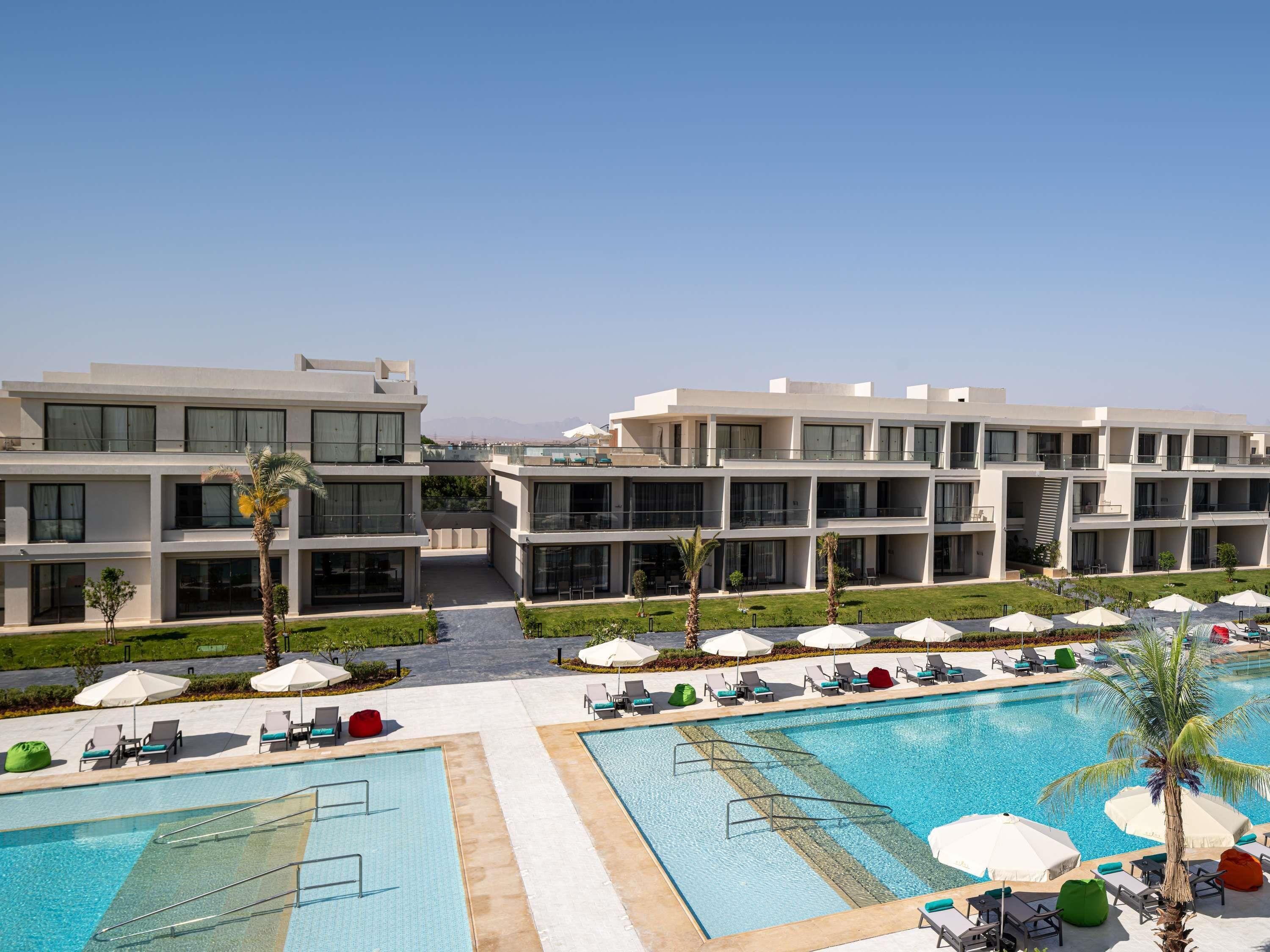 Un hotel moderno con area piscina, diversi balconi e cielo sereno.