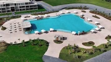 Vista aérea de un hotel con una piscina grande, tumbonas y una zona ajardinada.