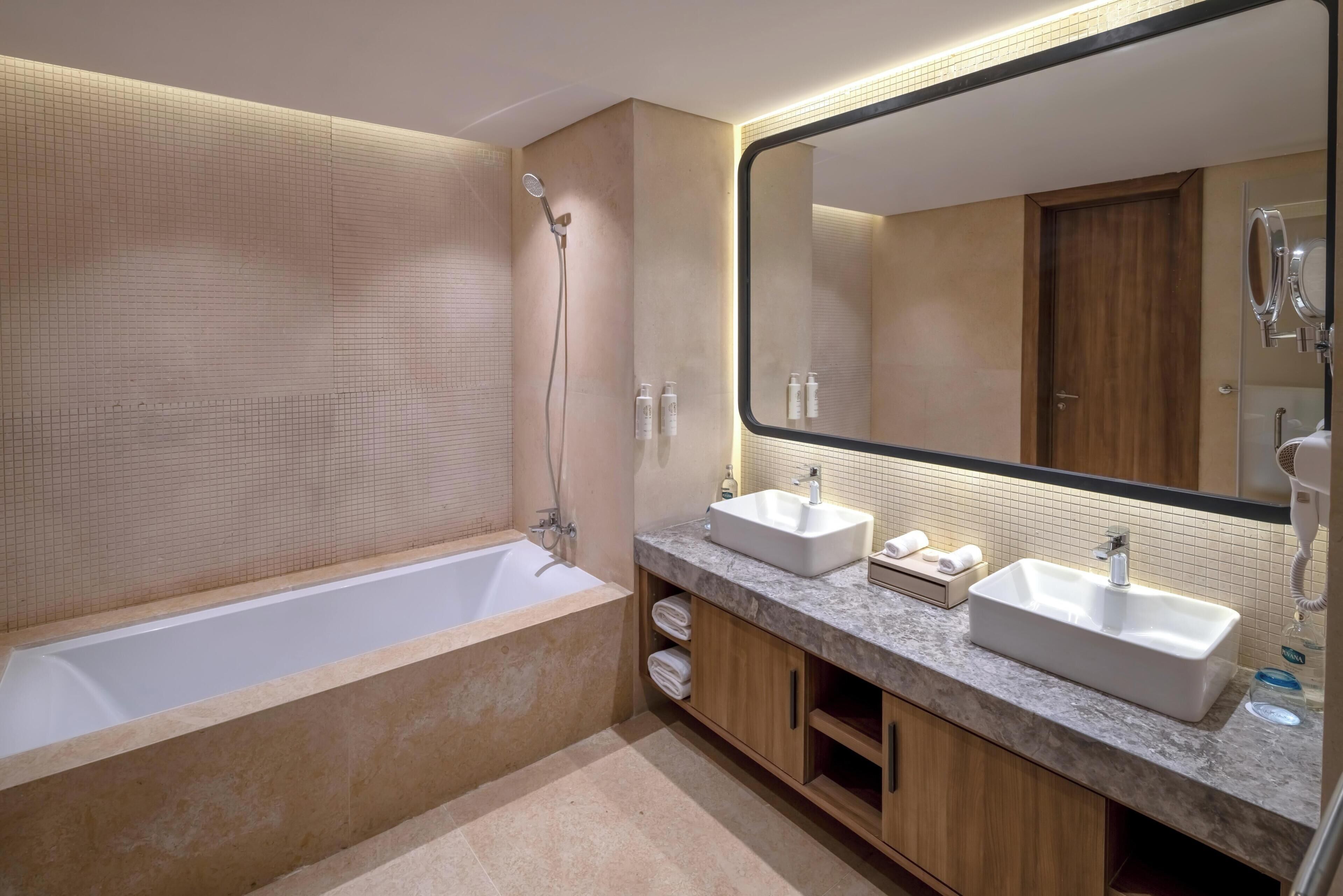 Une salle de bain moderne avec une baignoire, deux lavabos, un grand miroir et des meubles en bois.