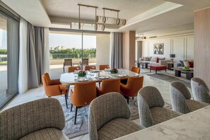 A modern dining area with a large table, orange chairs, and a view of the cityscape.