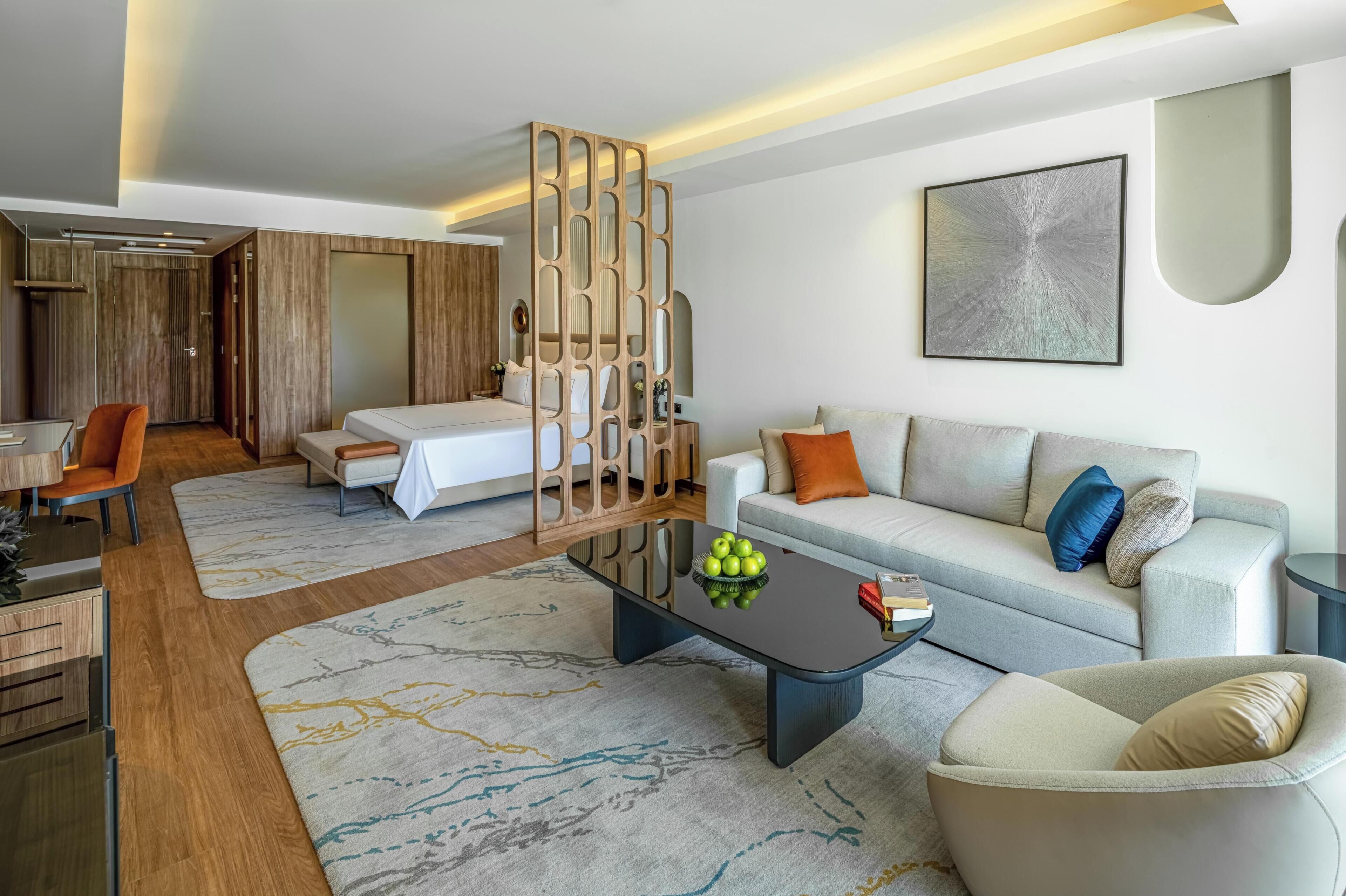 A modern hotel room with a bed, sofa, coffee table, and a decorative partition.