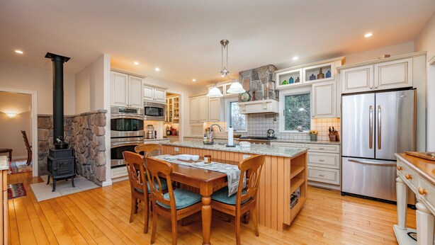 Cocina moderna con suelo de madera, una isla central, armarios blancos, electrodomésticos de acero inoxidable y una chimenea de piedra.