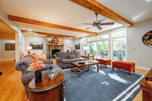 A spacious living room with a fireplace, large windows, and a ceiling fan. - New! Dog Friendly Lake Access Home w/ Hot Tub (Swanton)