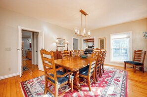 A dining room with a wooden table and chairs, a chandelier, and a large window. - New! Dog Friendly Lake Access Home w/ Hot Tub (Swanton)