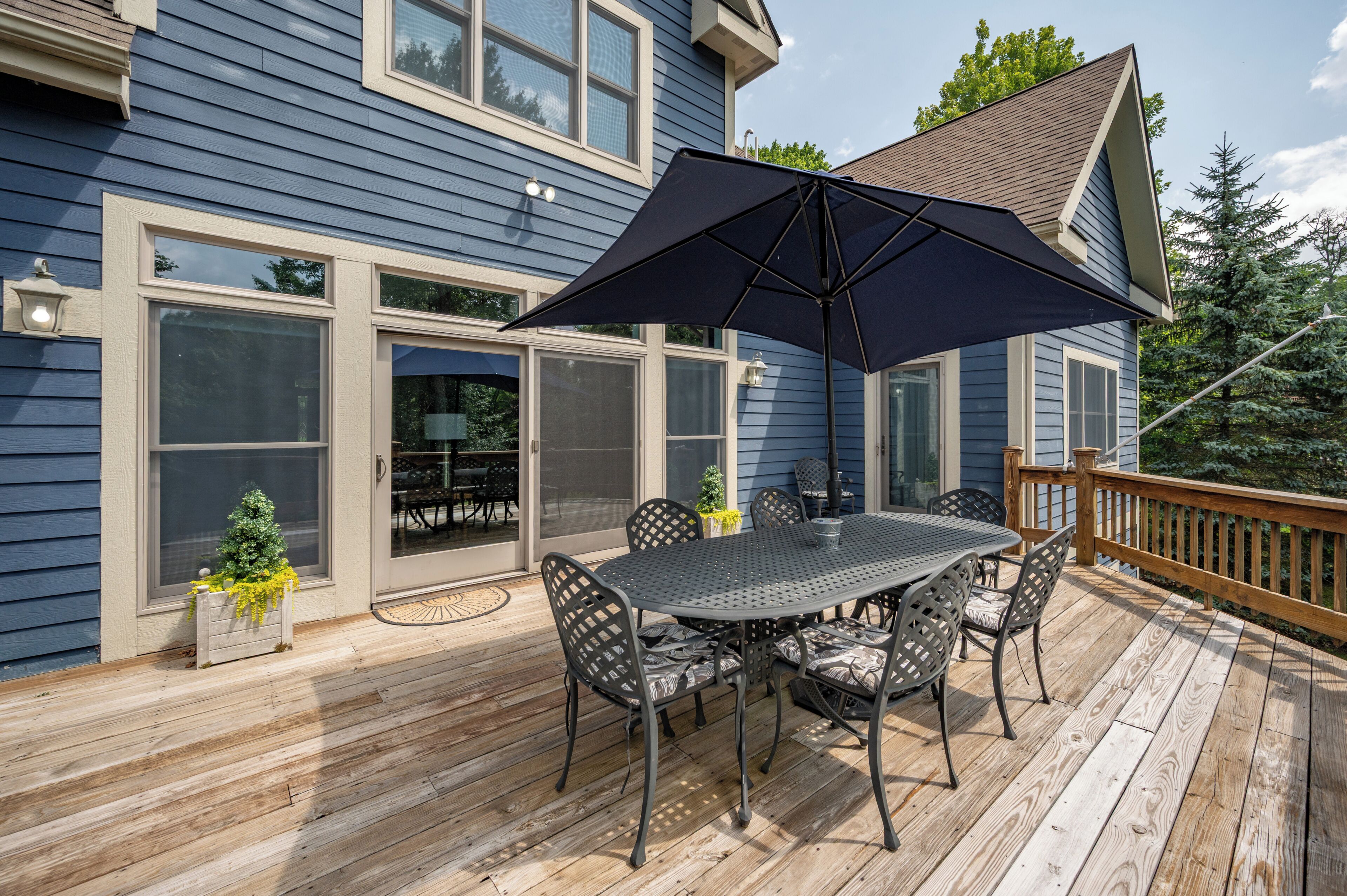 Una terraza con mesa y sillas, un parasol grande y una baranda de madera.