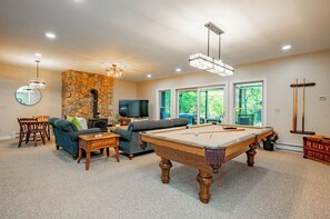 Una sala de estar con mesa de billar, área de descanso, pared de piedra y televisor.