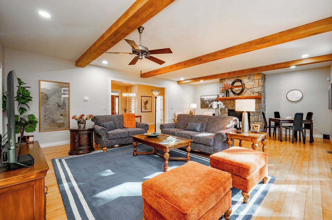 A spacious living room with a high ceiling, wooden beams, a ceiling fan, and a fireplace.