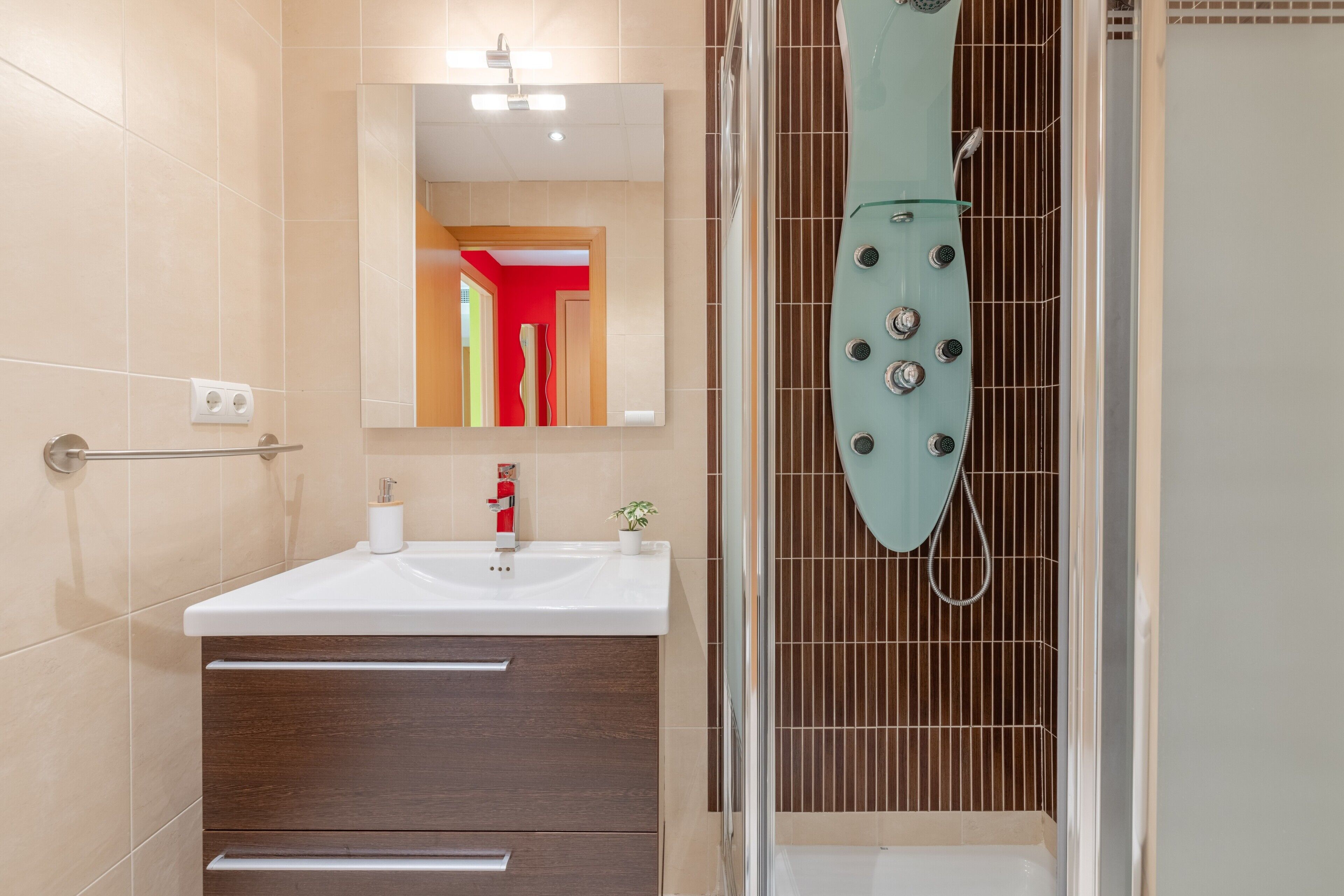 A modern bathroom with a glass shower enclosure, a white sink, and a mirror above it.
