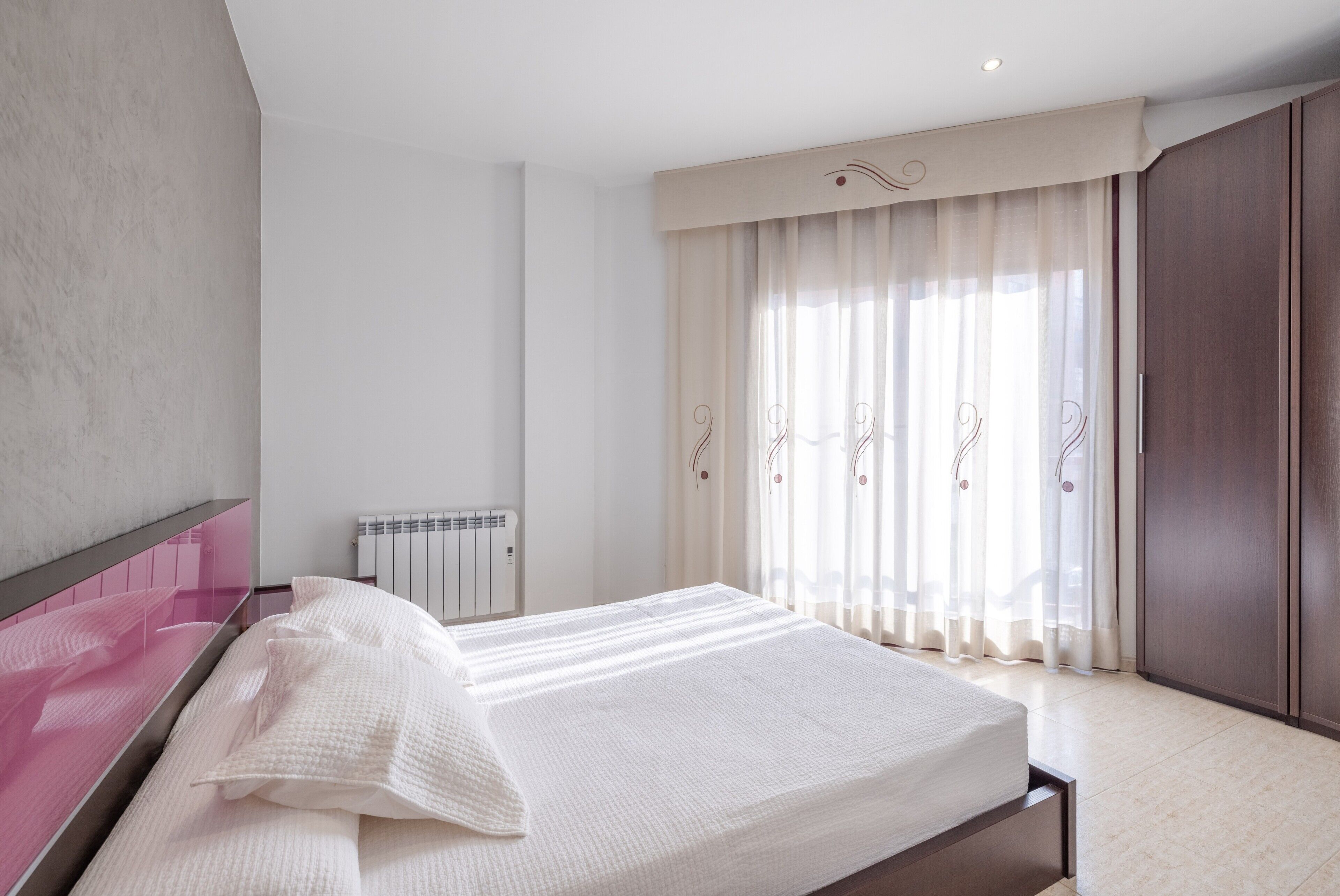 A bedroom with a bed, a radiator, curtains, and a wardrobe.