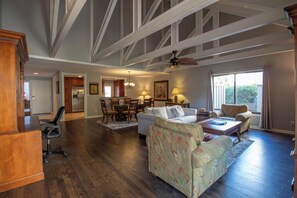 A spacious living room with hardwood floors, a white sofa, a floral armchair, and a dining area with a chandelier. - Dream Vacation House ~ community pool & near golf (Hilton Head Island)