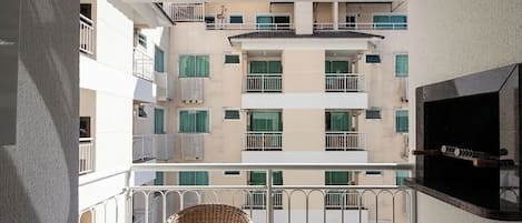 A multi-story building with balconies, a flat-screen TV mounted on the wall, and a wicker chair on the balcony.
