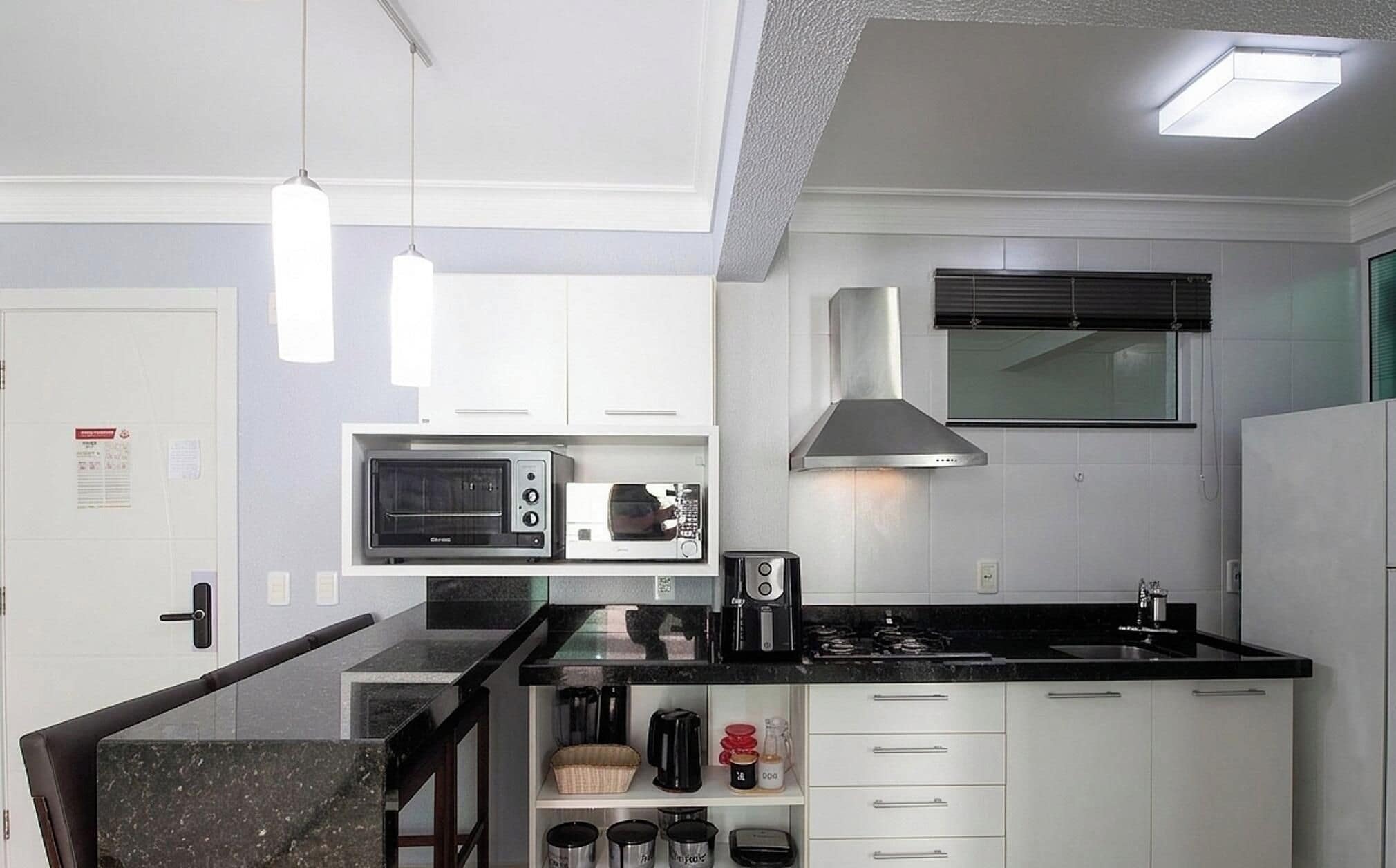 Una cocina compacta con armarios blancos, microondas, estufa y cafetera.