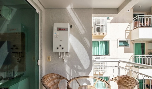 Un balcón con sillas de mimbre, calentador de agua y vistas a edificios vecinos.