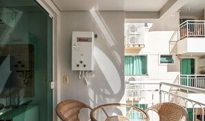 Een balkon met rieten stoelen, een boiler en uitzicht op omliggende gebouwen.