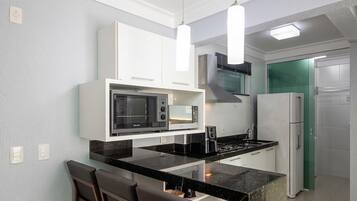 A compact kitchen with white cabinets, a black countertop, a microwave, a stove, and a refrigerator.