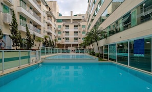 Una piscina rodeada por un edificio de varios pisos con balcones y fachada de vidrio.