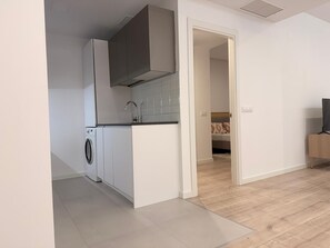 A modern kitchen with a washing machine, a built-in oven, and a small dining area with a TV. - Discover a space designed for comfortable and stylish Madrid living in the heart of Chamberí, one of the city's most authentic and charming neighborhoods. (MADRID)
