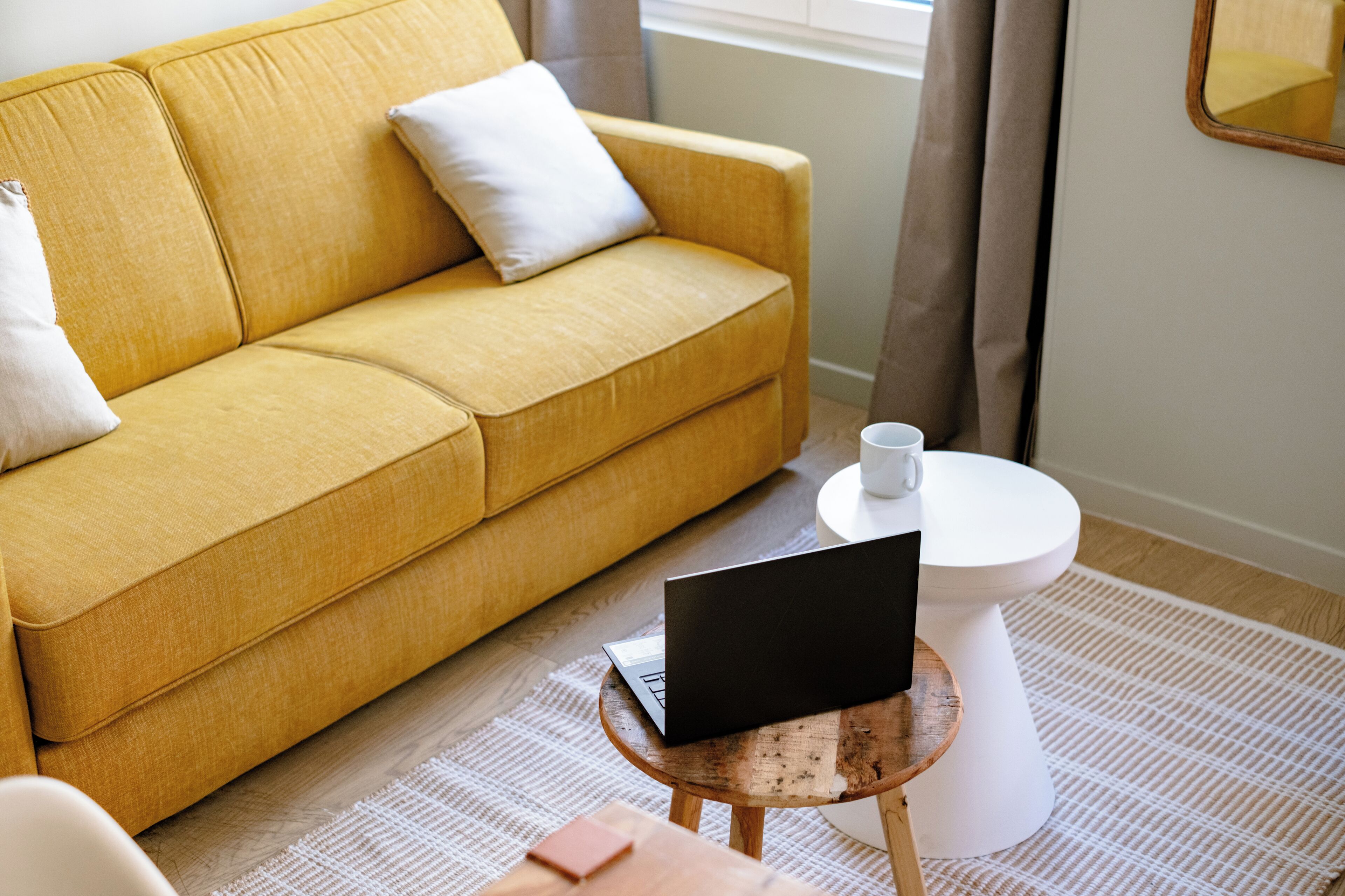 A yellow sofa with a laptop on a small wooden table, a white toilet, and a white cup on the floor.