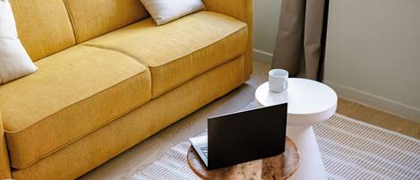A yellow sofa with a laptop on a small wooden table, a white toilet, and a white cup on the floor.
