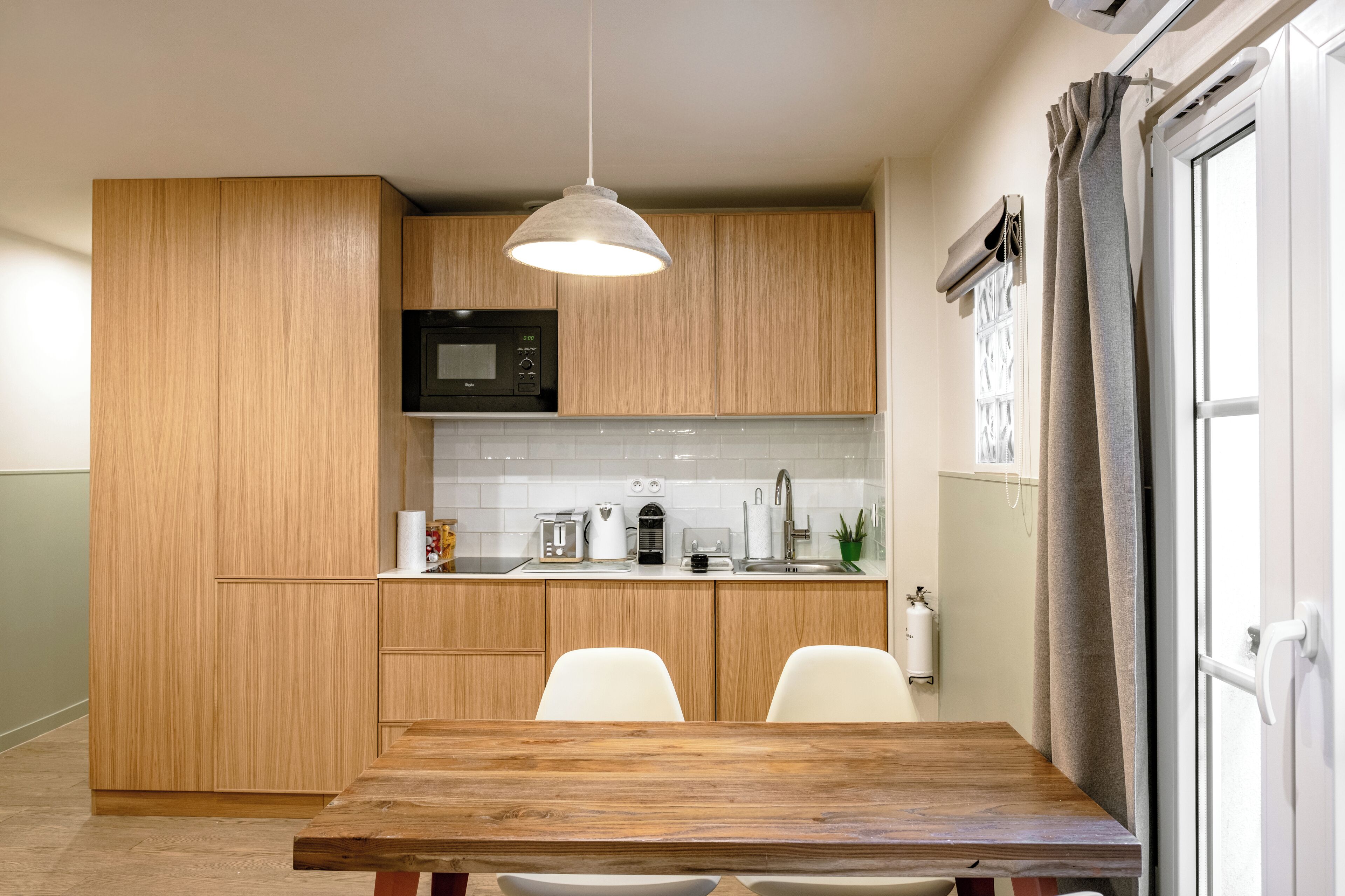 Une cuisine moderne avec des meubles de rangement en bois, un four à micro-ondes, un évier et une table à manger avec des chaises.