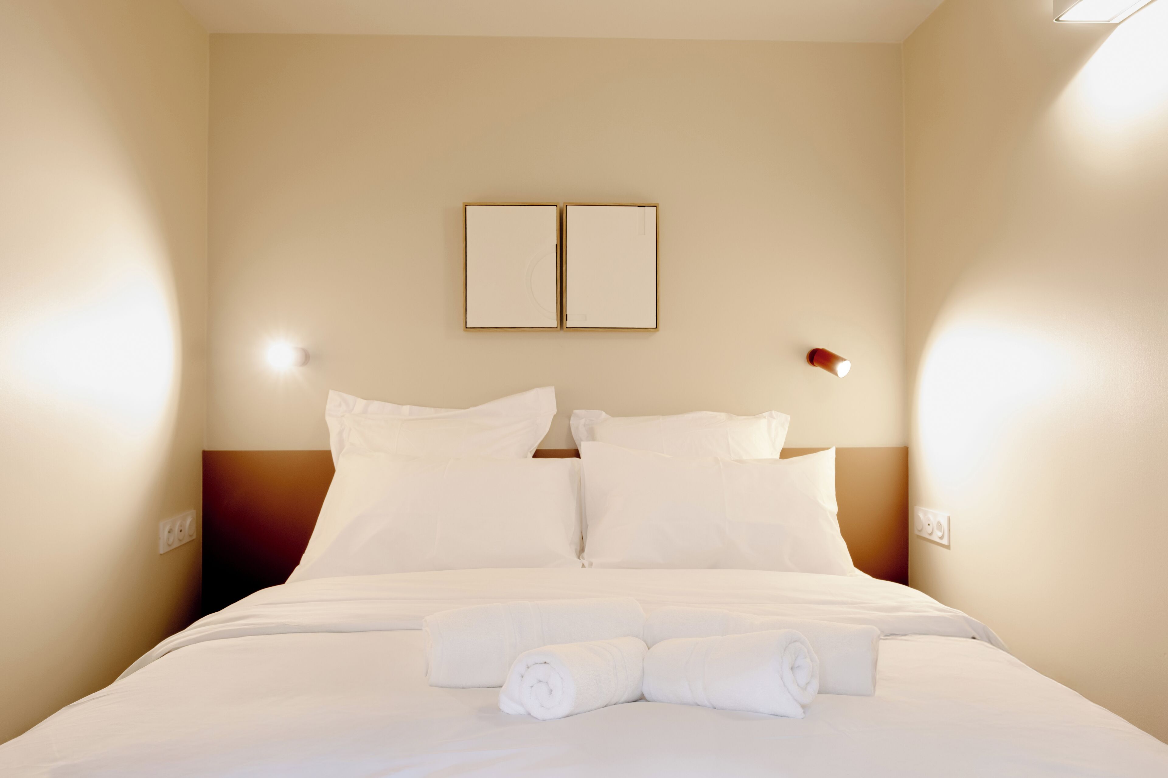 Ein Hotelzimmer mit einem ordentlich bezogenen Bett, zwei Nachttischen und einer Wandleuchte.
