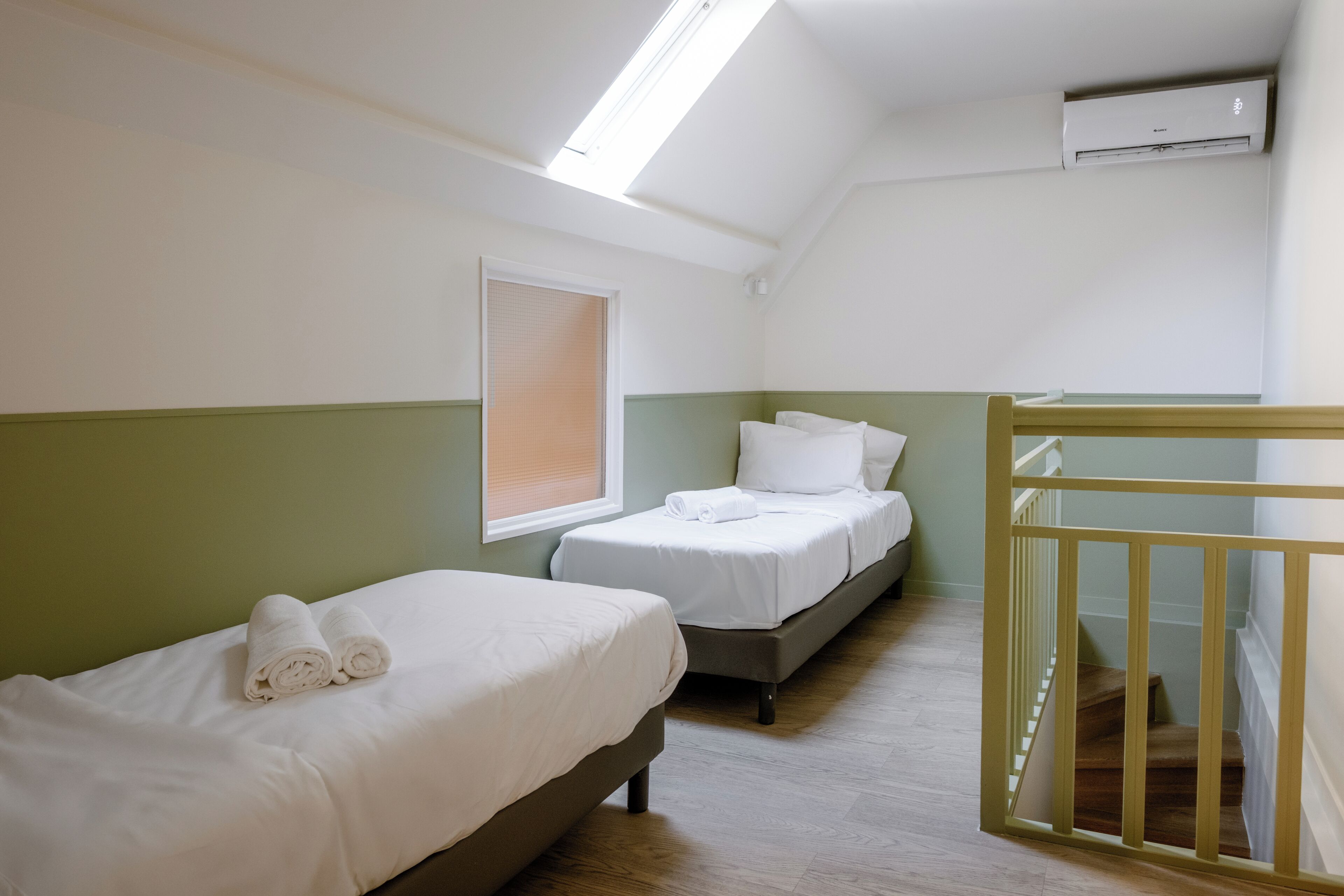 A room with two beds, a skylight, an air conditioning unit, and a wooden staircase.