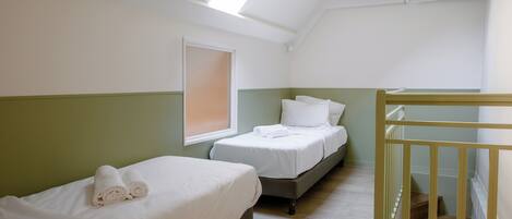 A room with two beds, a skylight, an air conditioning unit, and a wooden staircase.