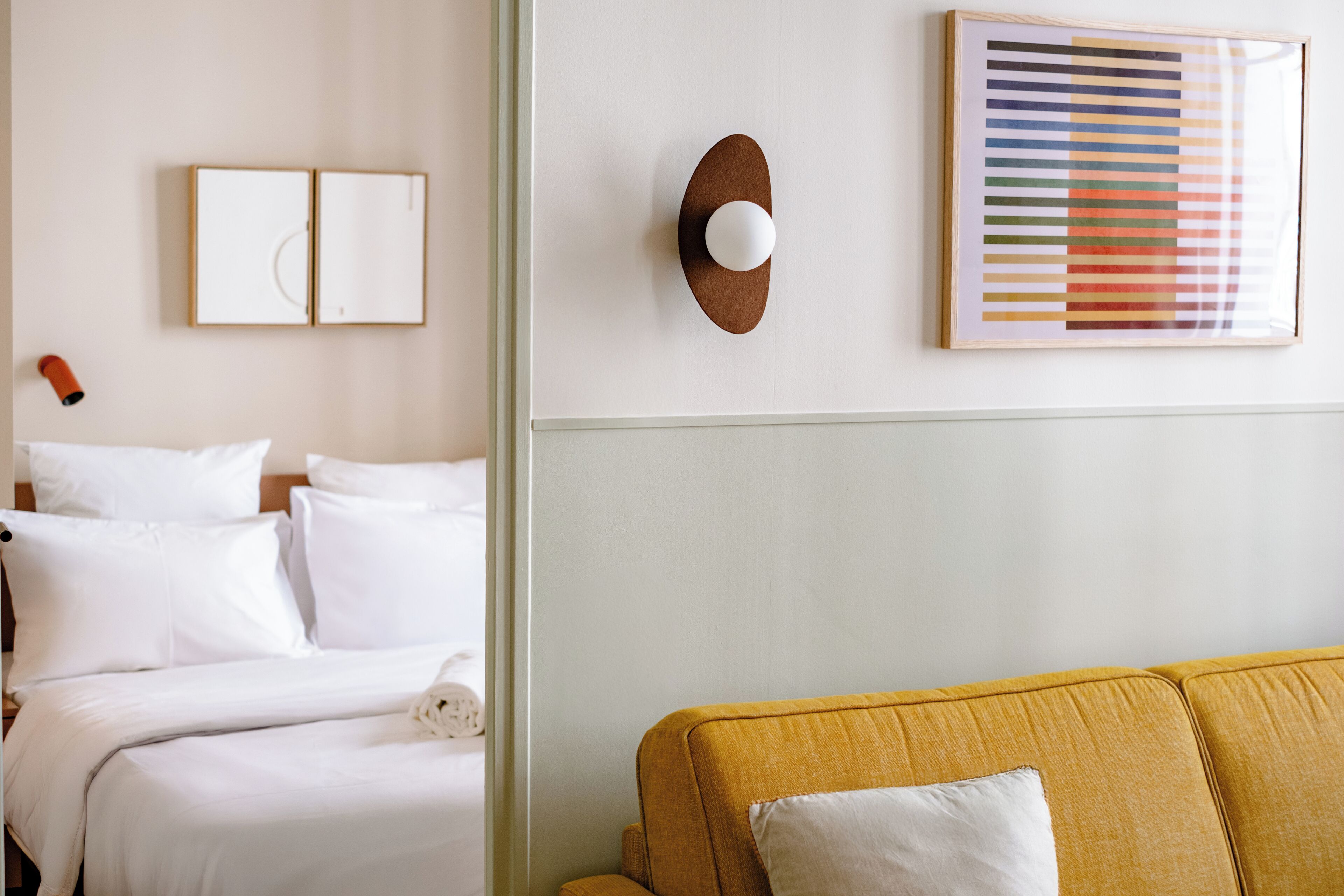 Quarto de hotel com uma cama, um sofá amarelo e uma obra de arte emoldurada na parede.