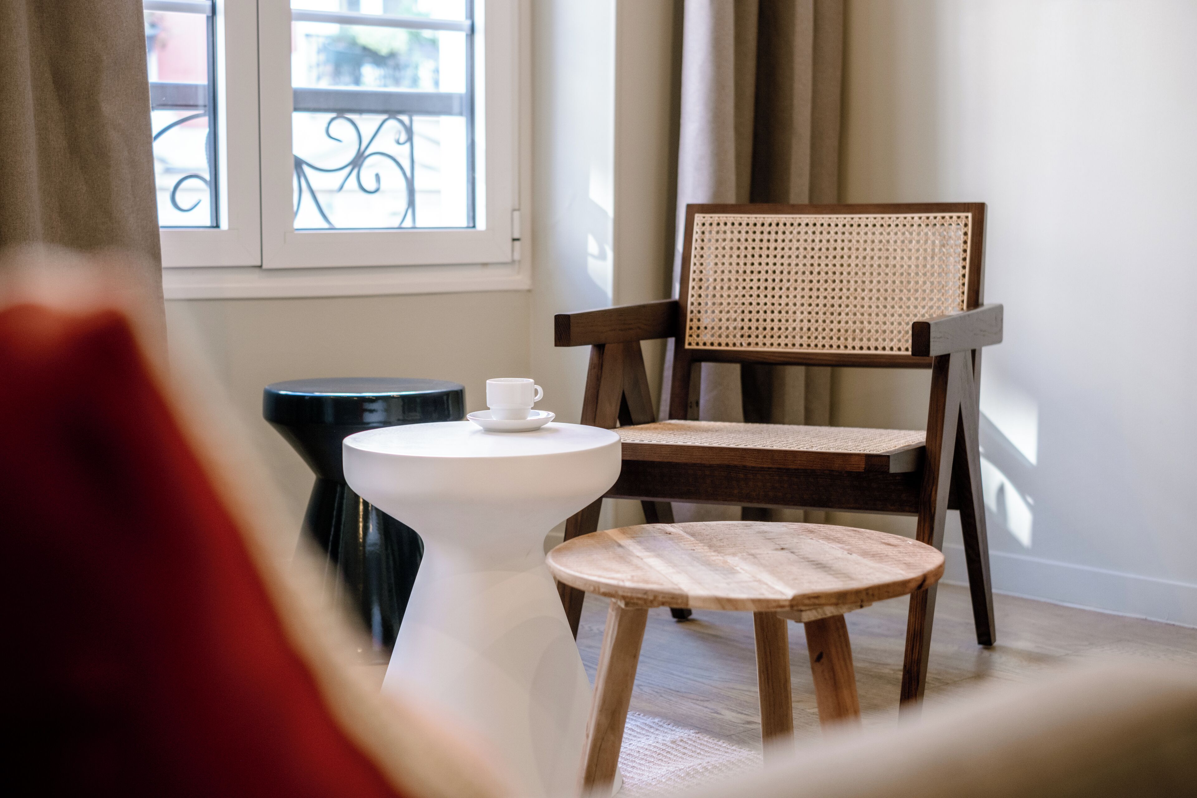 Una silla de madera con respaldo tejido, una mesa blanca con una taza y un taburete pequeño.