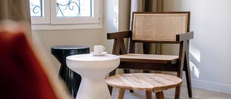 Una silla de madera con respaldo tejido, una mesa blanca con una taza y un taburete pequeño.