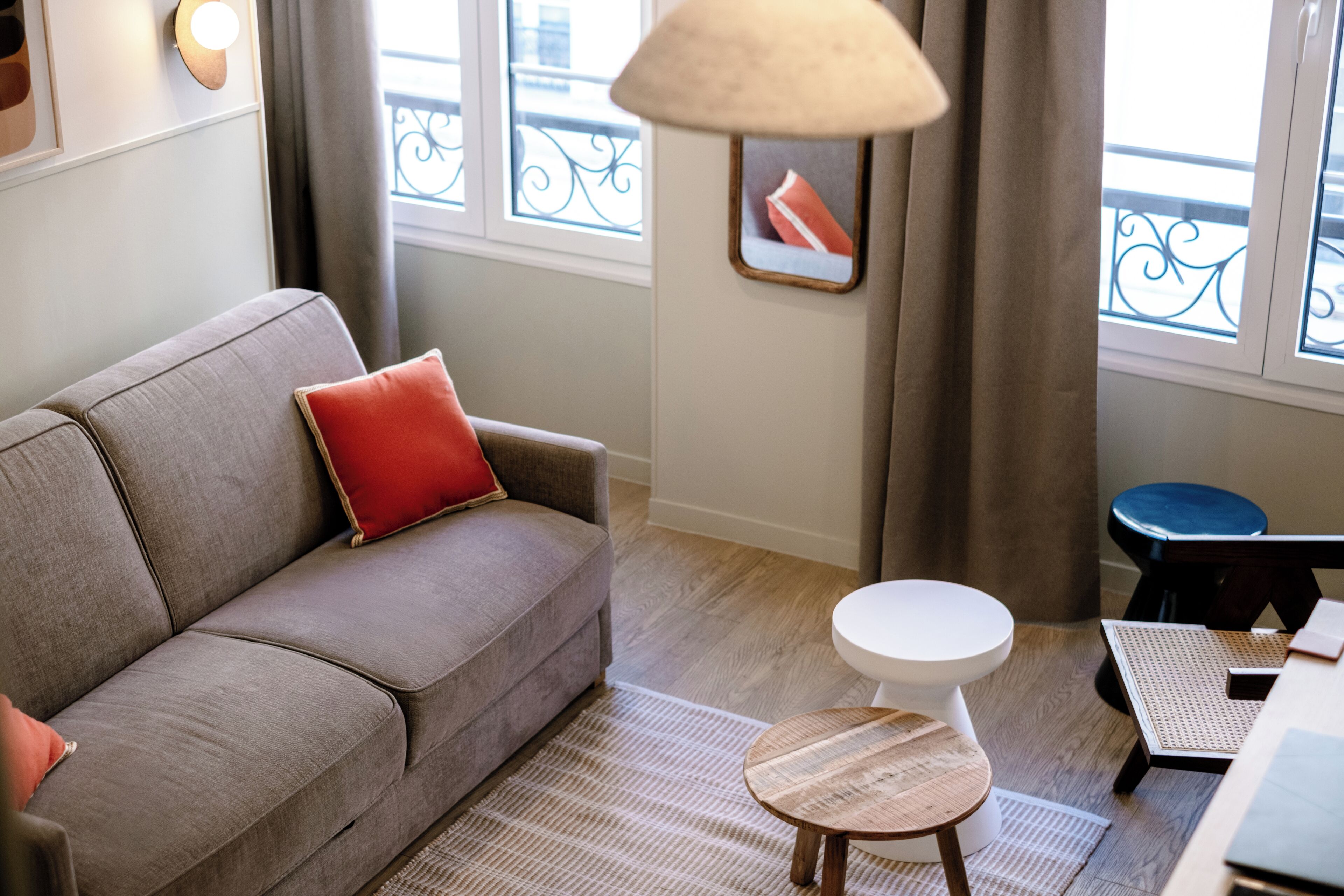 Ein modernes Wohnzimmer mit einem grauen Sofa, einem kleinen runden Tisch und einem Fenster mit Blick auf den Balkon.