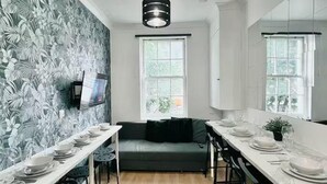 A modern kitchen with a long dining table, a sofa, and a TV mounted on the wall. - Comfortable 3 Bed Flat in King Cross (London)