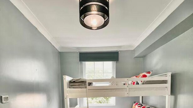 A bunk bed room with a ceiling fan, a window, and a small bedside table. - Comfortable 3 Bed Flat in King Cross (London)