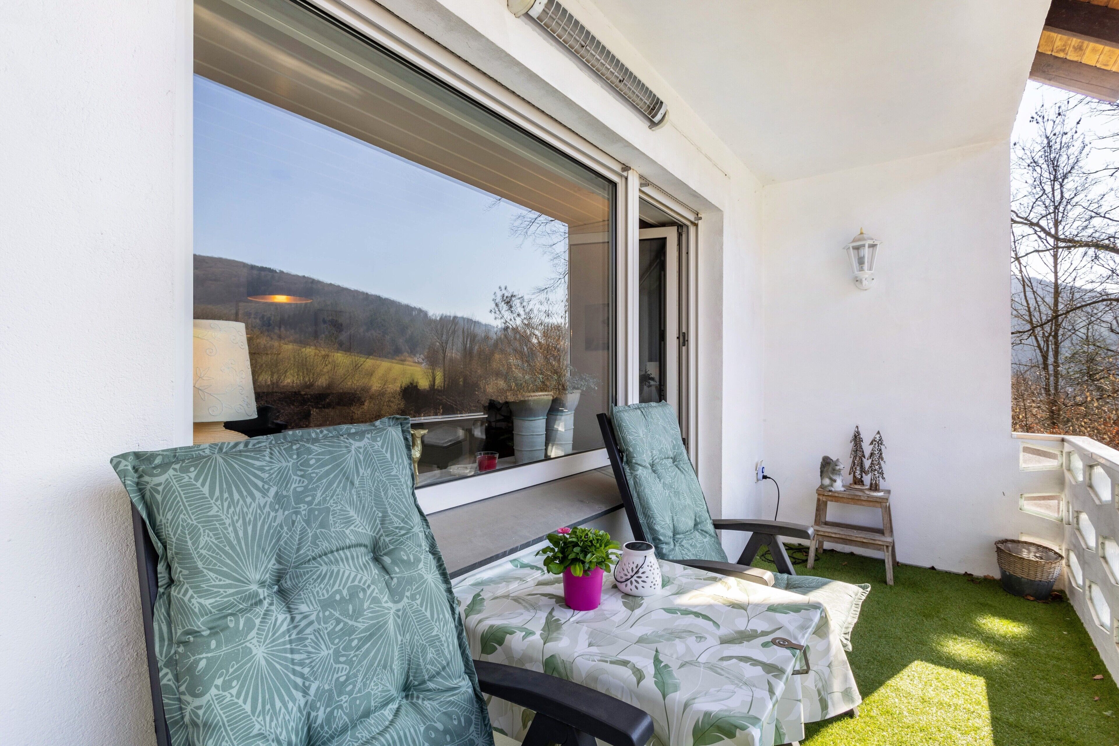 A balcony with two chairs, a small table, a potted plant, and a decorative item.