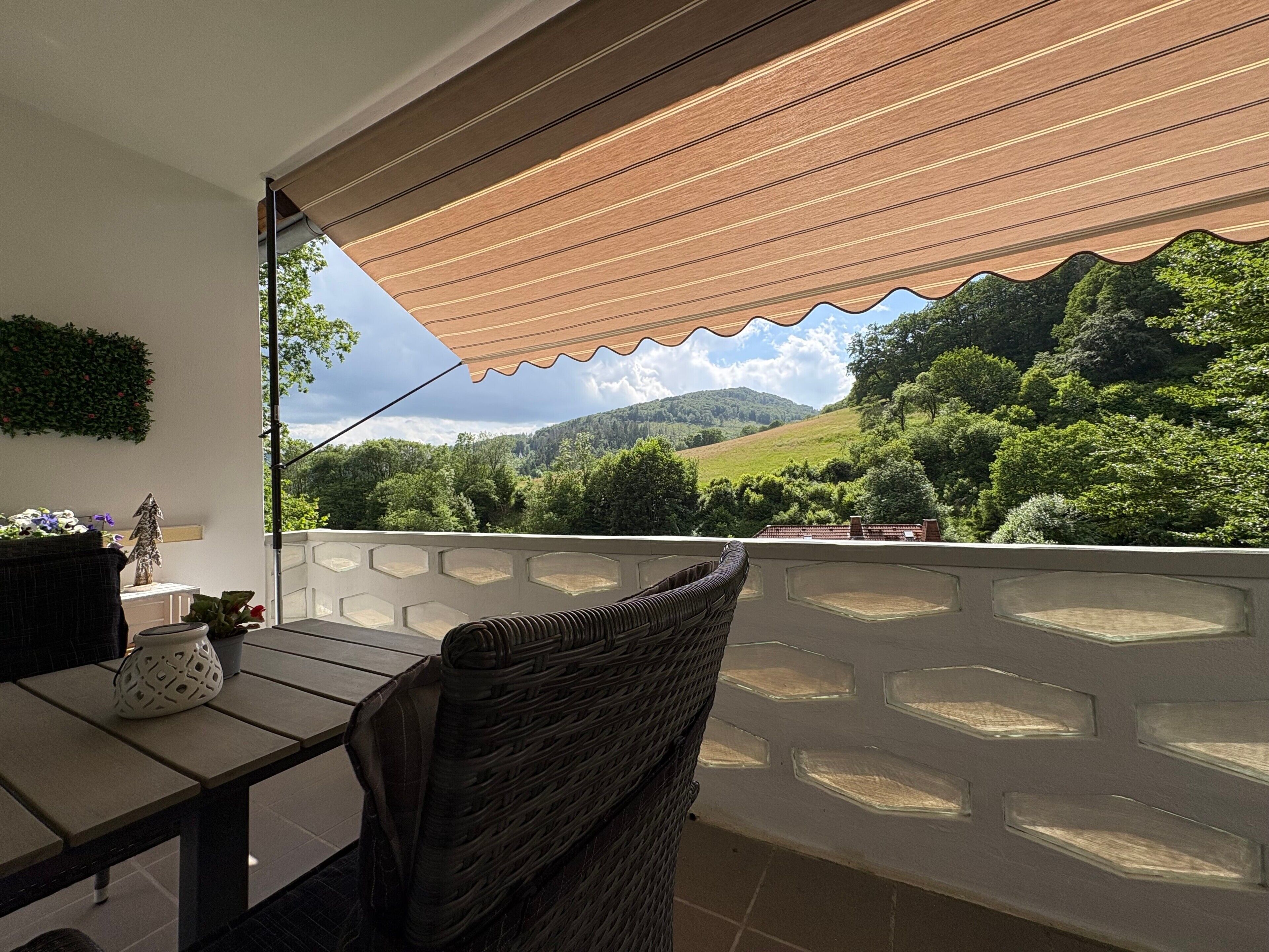 Un balcón con vistas a un paisaje verde, una mesa con sillas y una planta decorativa.