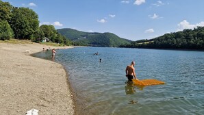 Un lac où l’on peut se baigner et où des gens se promènent le long de la rive, le tout étant entouré de collines.