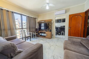 A living room with a TV, sofa, and dining area. - Apto Pet Friendly Beira-mar c Garagem no Boqueirão (Praia Grande)