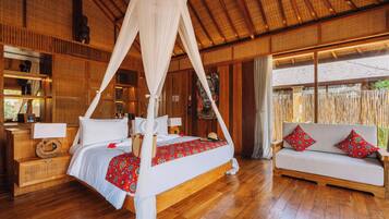 A room with a four-poster bed, a sofa, wooden flooring, and a thatched roof.