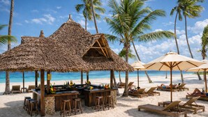 Un bar de playa con techo de paja, sillones de madera y sombrillas.
