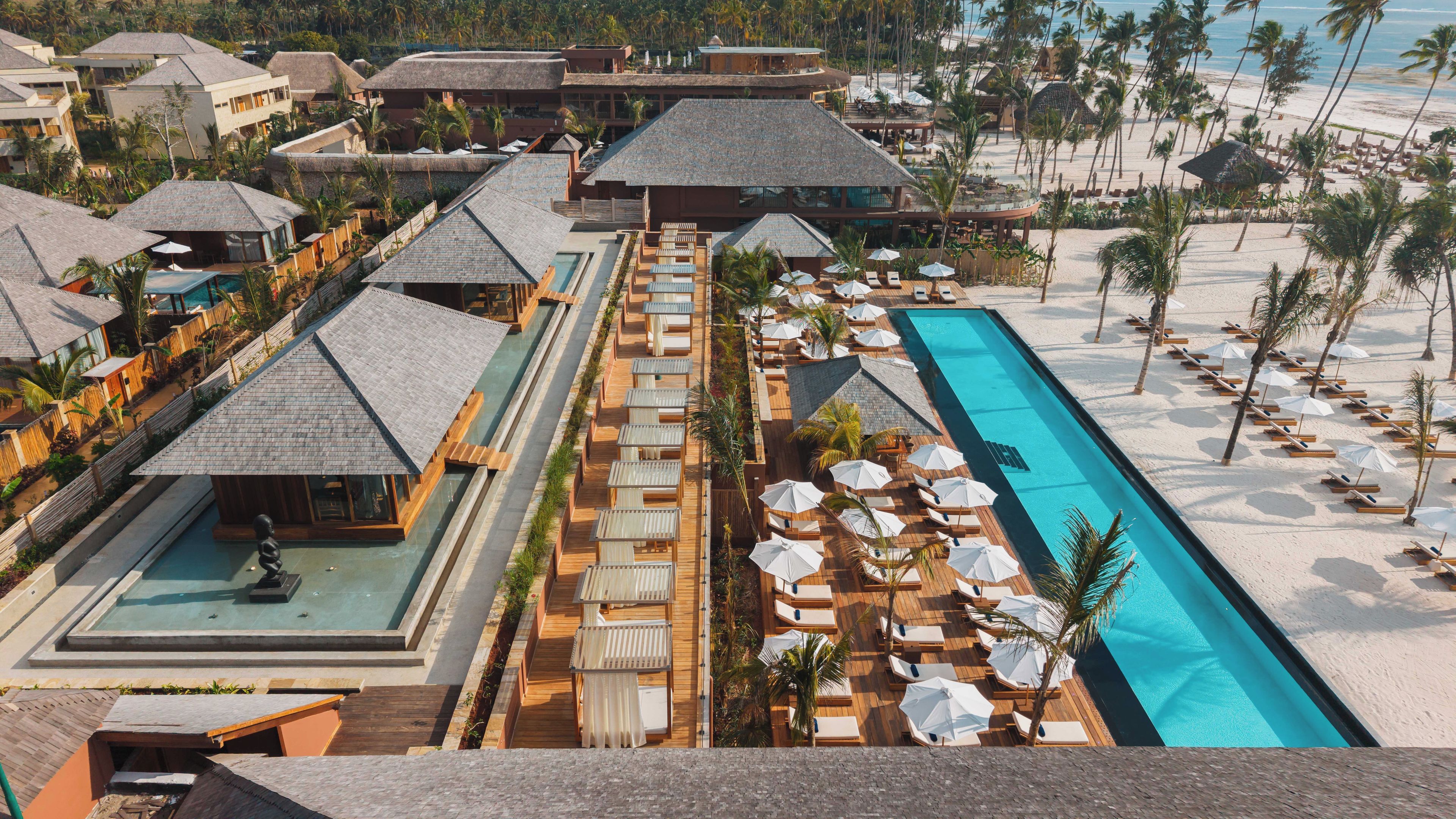 Een resort met meerdere bungalows op palen, een centraal zwembad en een strandgedeelte.