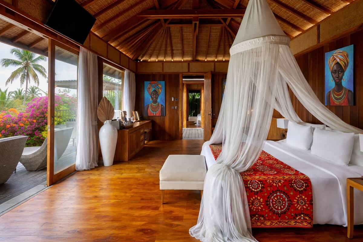 Ein Schlafzimmer mit Baldachinbett, Holzboden, Schreibtisch mit einer Vase und Kunstwerken an den Wänden.