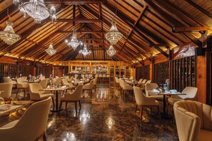 Un restaurant spacieux avec de hauts plafonds en bois et des lustres. Les tables sont disposées avec des chaises, et le sol est recouvert de marbre poli.