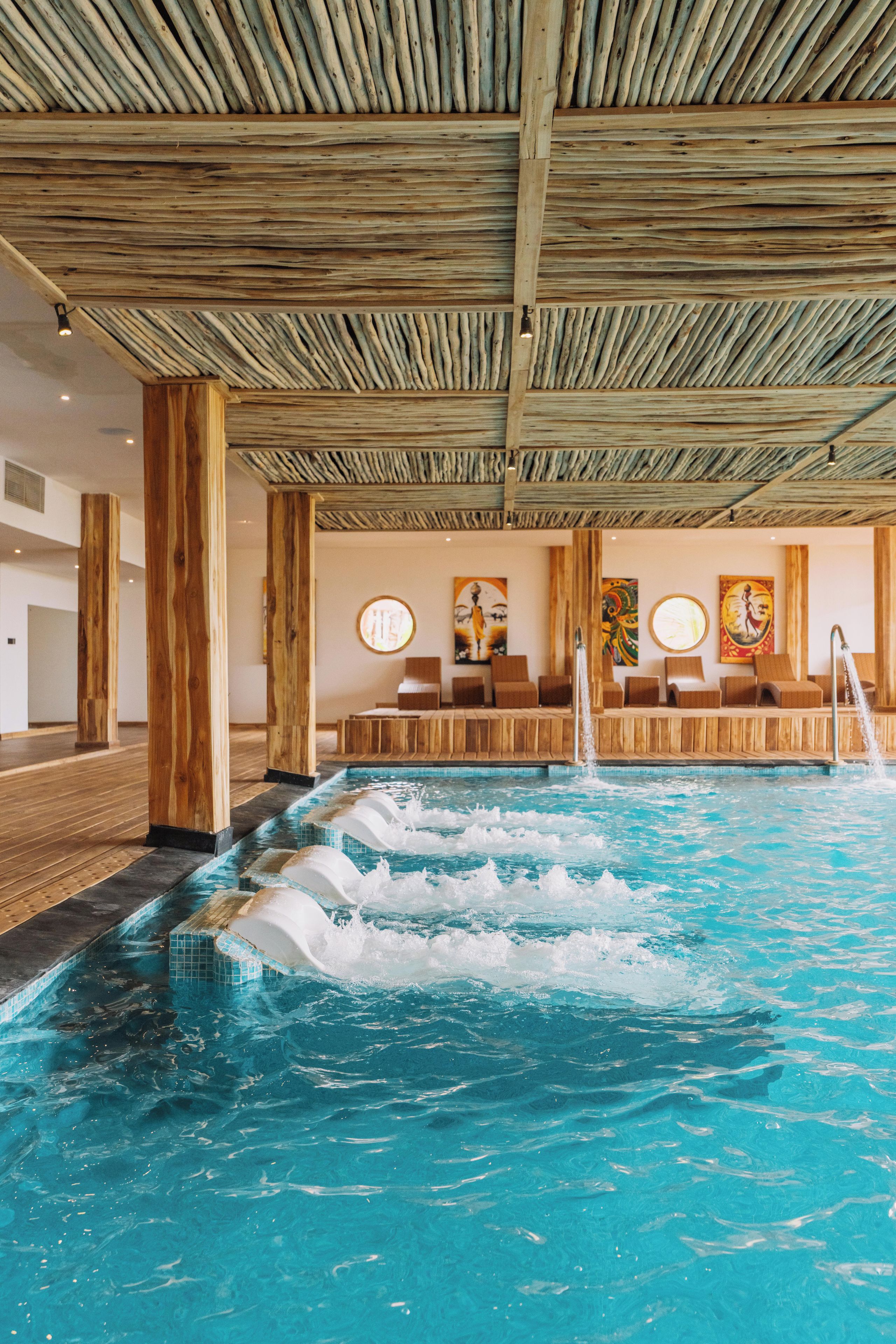 An indoor swimming pool with wooden beams overhead and a seating area with artwork on the walls.
