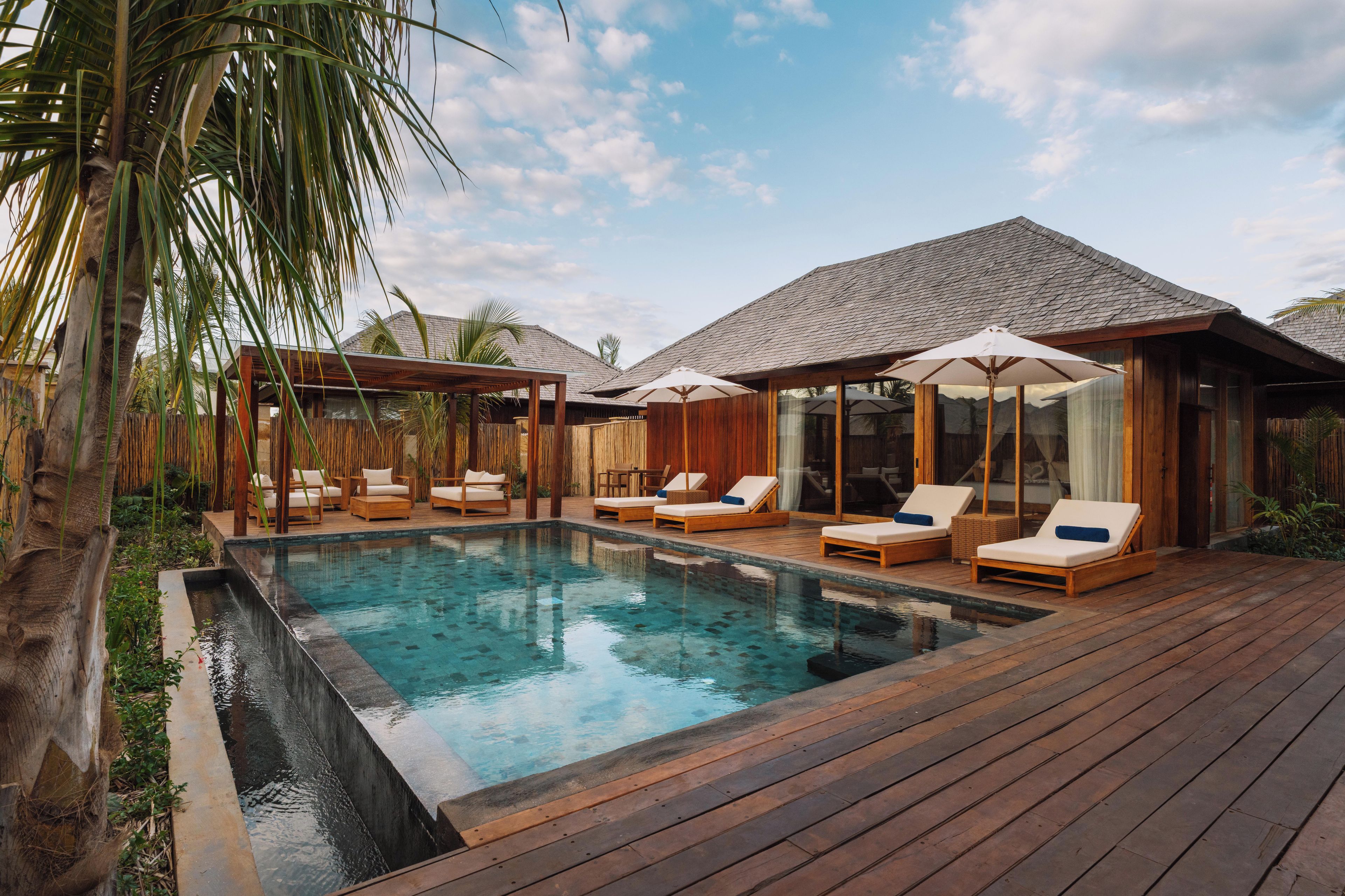 A pool area with wooden deck, lounge chairs, and umbrellas.