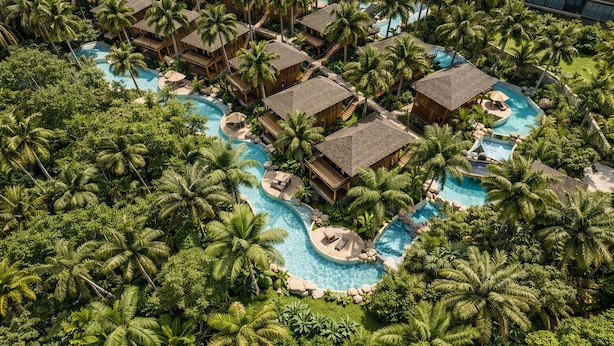 Vista aérea de un resort con varias cabañas, una piscina central y exuberante vegetación tropical.
