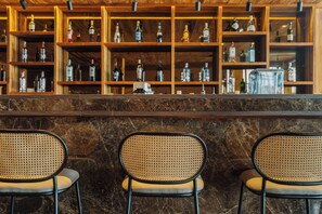 Een bar met een marmeren toonbank en drie rieten stoelen.