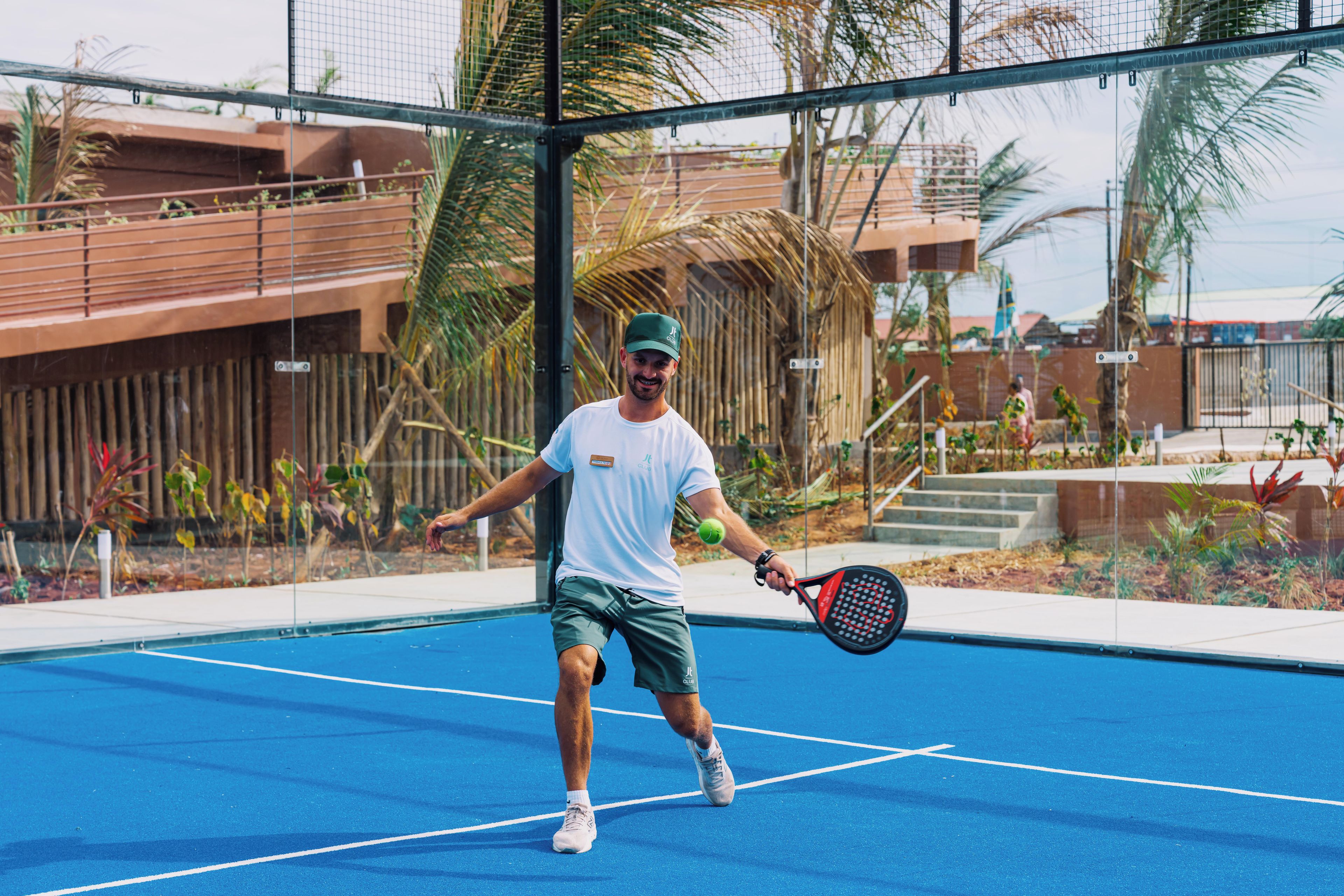 A tennis court with a net, palm trees, and a building in the background.