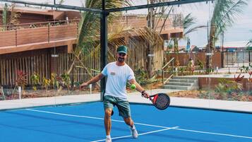 A tennis court with a net, palm trees, and a building in the background.