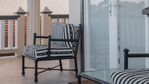A balcony with a chair and a table, a glass door, and a view of a building in the background. - Stylish 1BR with Patio, Pool & Marina View in Rodney Bay (Rodney Bay)