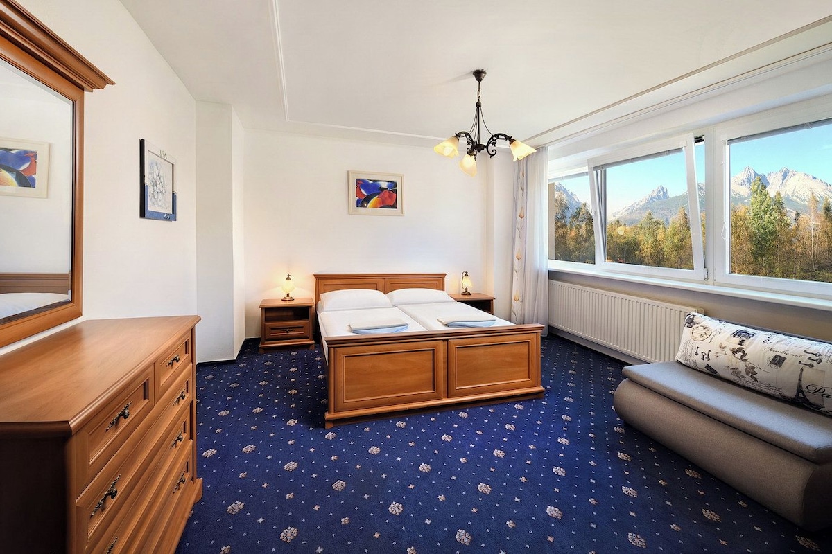 Ein Schlafzimmer mit Bett, Schminktisch, Nachttischen und Blick auf Berge durch das Fenster.